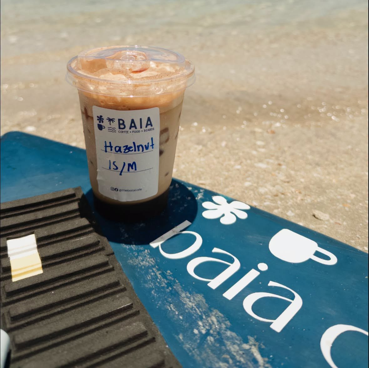 BAIA Hazelnut Iced Coffee and custom branded skimboard on the beach sand